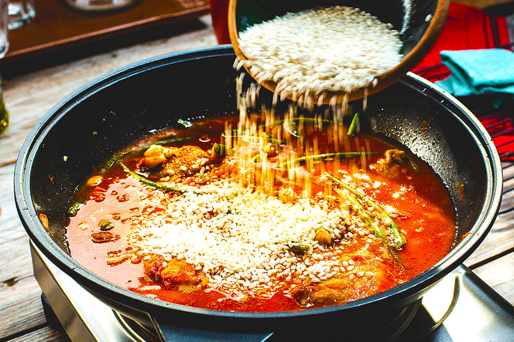 In eine Pfanne mit Paella wird Reis gegeben