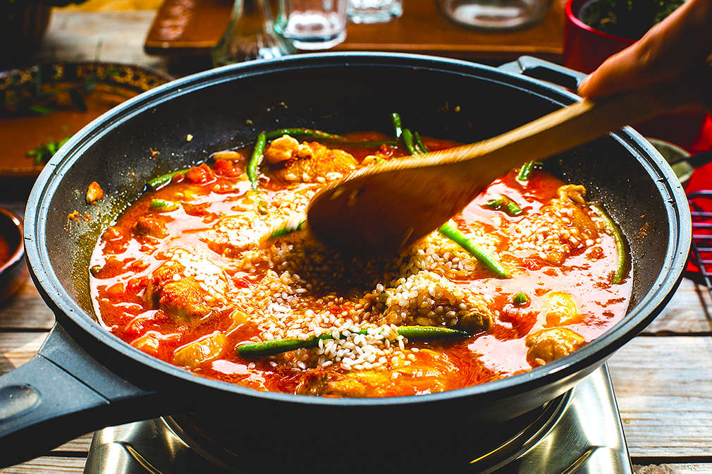 In eine Pfanne mit Paella wird ein Löffel gehalten