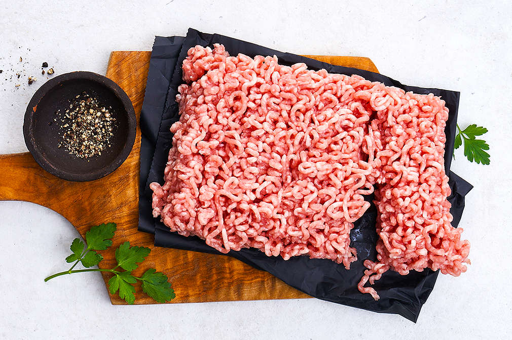 Hackfleisch, das auf eine schwarze Serviette auf einem Holzbrett gelegt wurde; auf dem Holzbrett befinden sich außerdem einige Blättchen Petersilie sowie eine kleine schwarze Schale mit Pfeffer