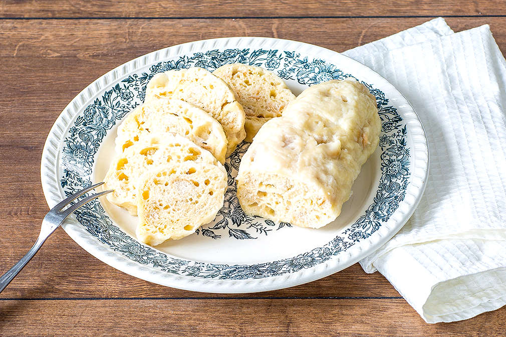 Zwei aufgeschnittene Böhmische Knödel liegen auf einem Teller, daneben eine Gabel und eine weiße Serviette