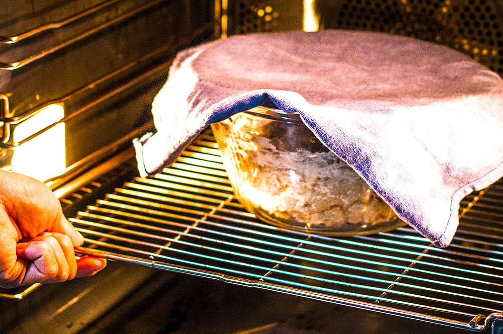 Eine zugedeckte Schüssel mit Hefeteig steht auf einem Rost im Backofen.