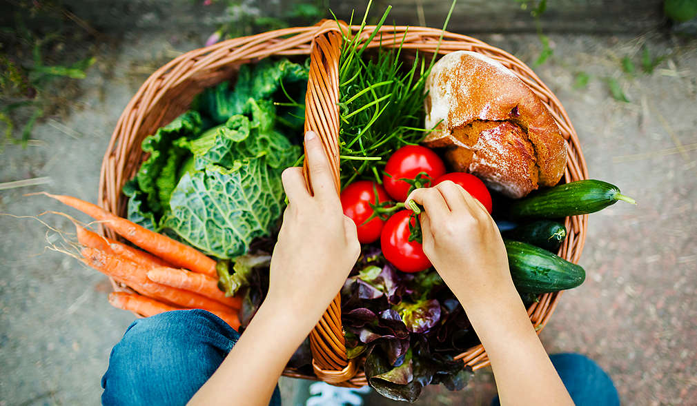Person mit Korb voller Gemüse und Brot