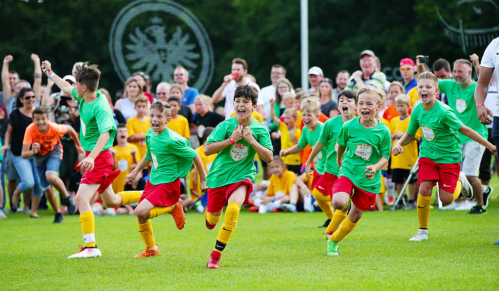 Kinder in Trikots rennen über Fußballplatz, freuen sich und jubeln