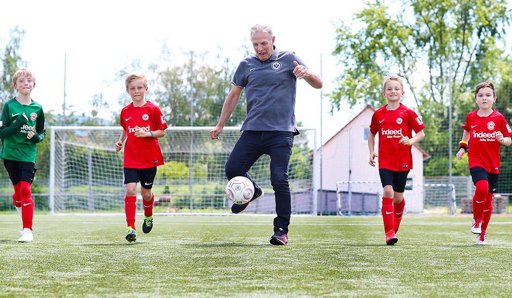 Kinder laufen auf dem Fußballplatz neben Fußballspieler Charly Körbel