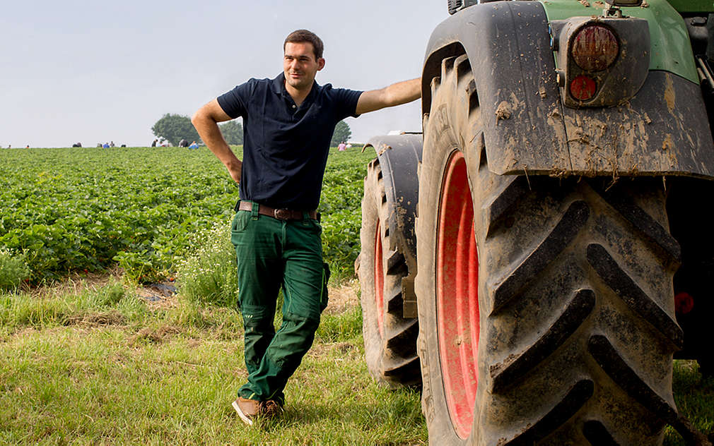 Muž se opírá o traktor zaparkovaný na poli