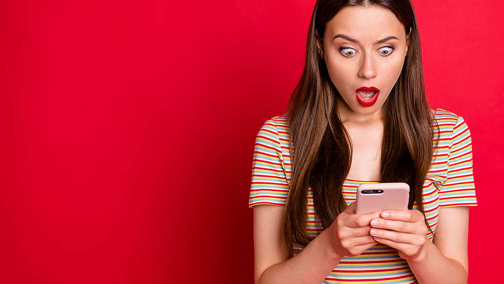 Eine Frau schaut begeistert auf ihr Smartphone