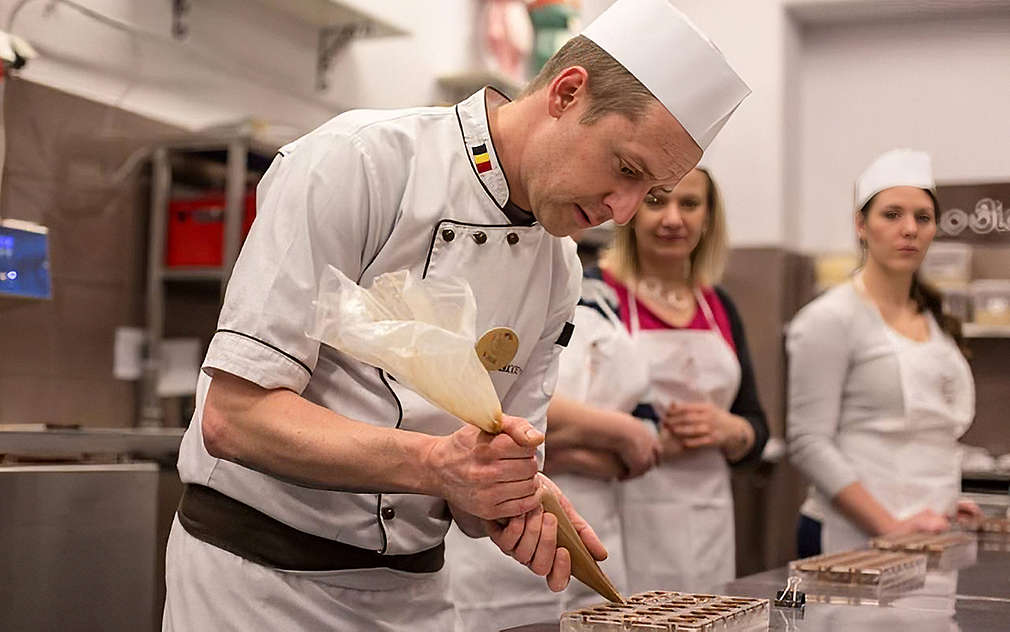 cukrář klade čokoládu do připravených formiček na pralinky před účastníky kurzu