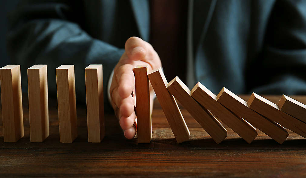 Hand hält Dominosteine von weiterem Umfallen auf