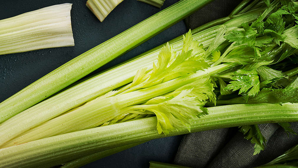 Svetlý podklad, stonkový zeler, ktorý leží ovinutý servítkou na tanieri. Smerom k stonke je nakrájaný na malé kúsky.