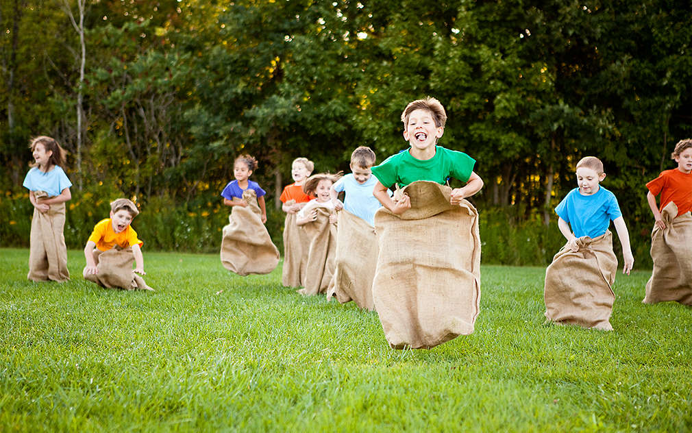 Grupa dzieci organizuje zawody skakania w workach na łące.