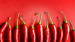 Više čili paprika raspoređenih jedna pored druge na crvenoj pozadini