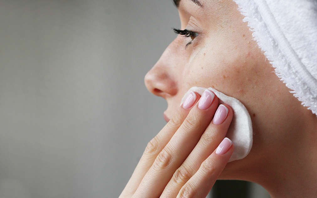 Detailní záběr na ženu, která si otírá obličej vatovým tamponkem.