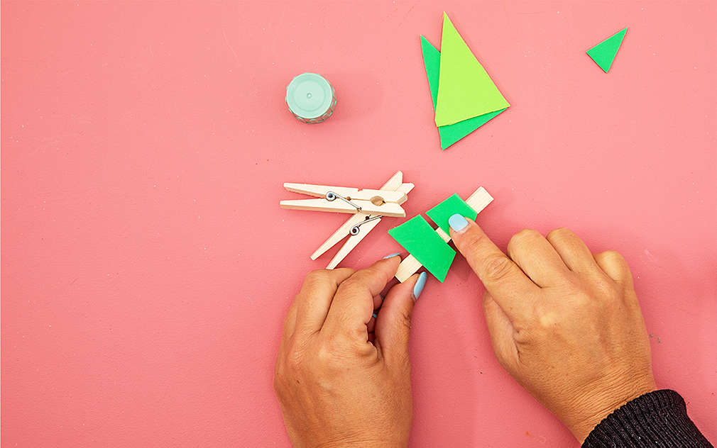 Dve ruky na ružovom podklade lepia na štipce zelené kúsky mäkkej penovej gumy, takže vznikajú malé jedličky.