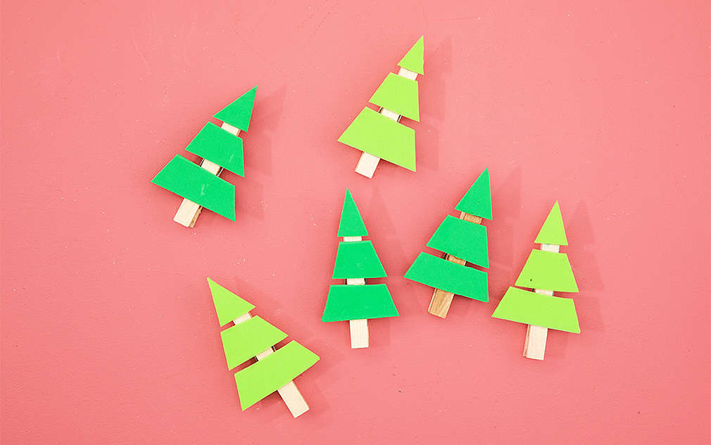 Šesť vianočných stromčekov vyrobených z penovej gumy a štipcov v dvoch rôznych odtieňoch zelenej na ružovom podklade.