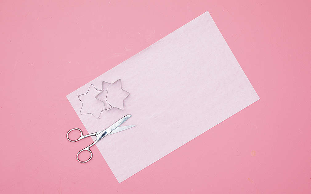 Desiatový papier, formičky na sušienky a nožnice sú položené na ružovom podklade.