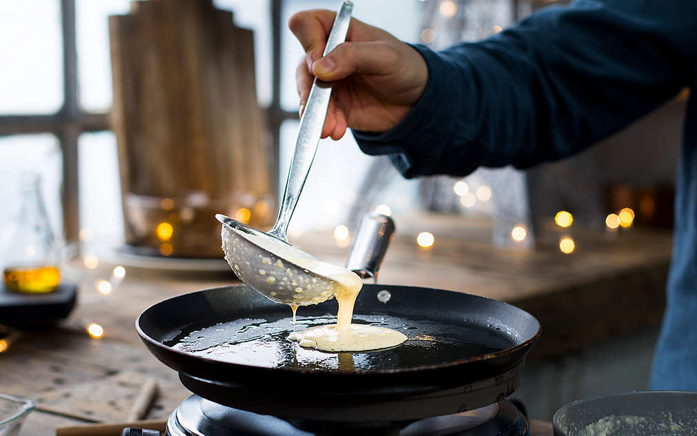 Tekuće tijesto grabilicom se ulijeva u plitku tavu za palačinke s uljem.