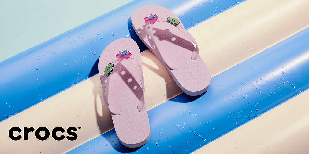 Jasnoróżowe klapki Crocs na materacu plażowym
