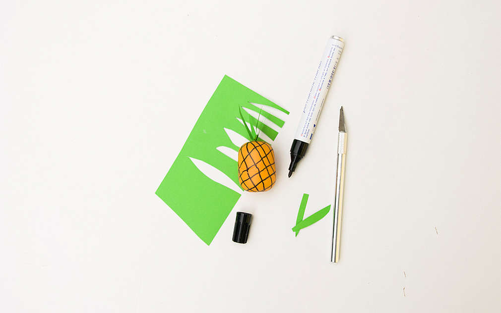 Se confecționează un ananas dintr-o hârtie verde și o capsulă de plastic de la un ou cu surprize, pe care a fost desenat cu un pix negru modelul specific.