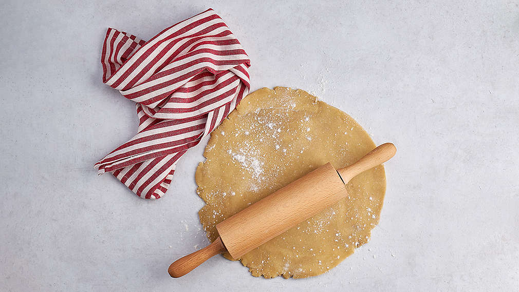 Ausgerollter Teig, darauf ein Nudelholz, daneben ein weiß-rot gestreiftes Küchentuch., Ausgerollter Teig, darauf ein Nudelholz, daneben ein wei�-rot gestreiftes K�chentuch.