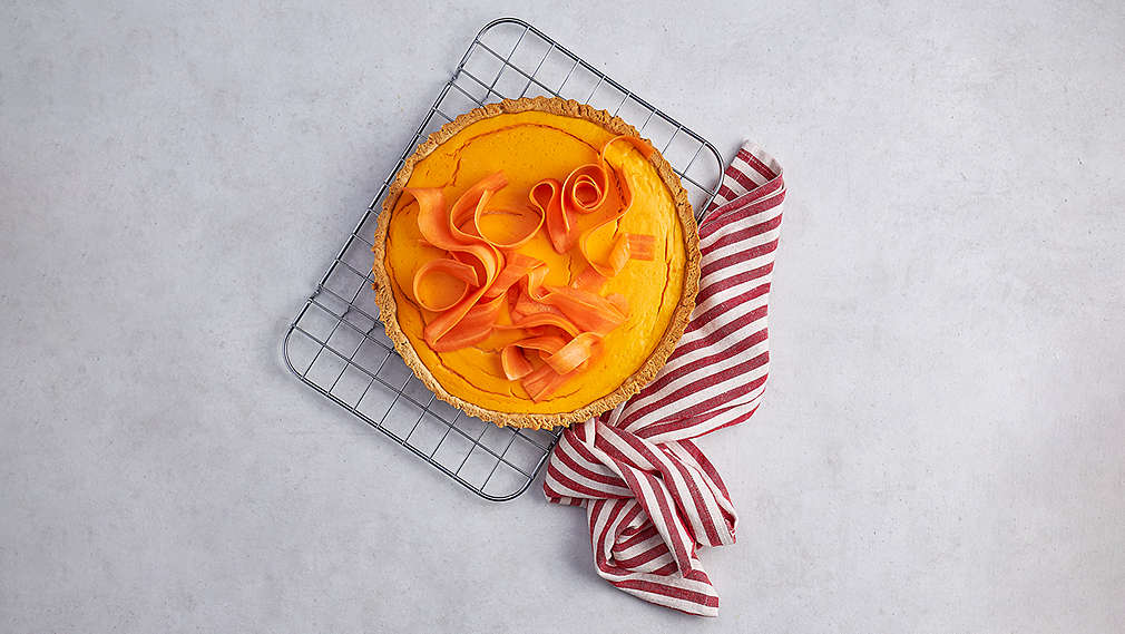 Fertige Tarte mir Möhrenverzierung auf einem Rost, daneben ein  weiß-rot gestreiftes Küchentuch., Fertige Tarte mir M�hrenverzierung auf einem Rost, daneben ein  wei�-rot gestreiftes K�chentuch.