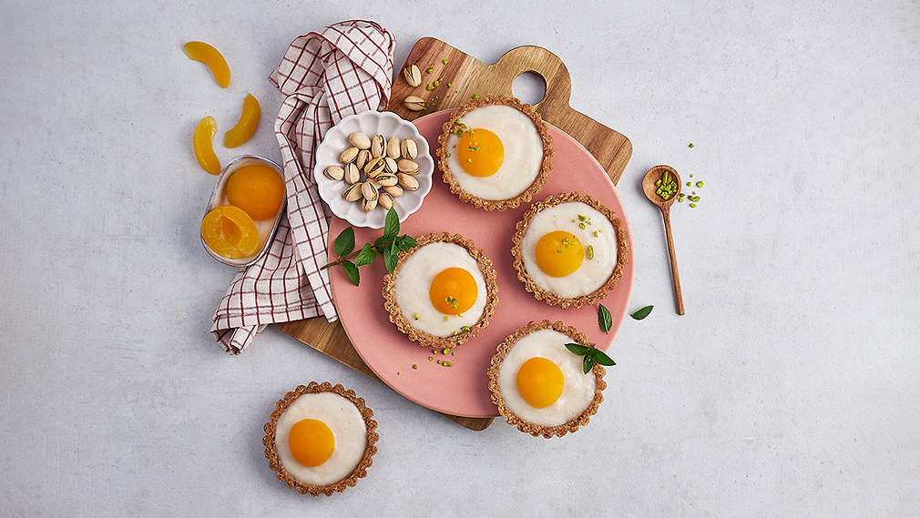 Kleine, runde, gefüllte Teigformen auf einem Holzbrett, geschmückt mit Aprikosen. Daneben ein karriertes Küchentuch sowie eine Schüssel mit Aprikosen. , Kleine, runde, gef�llte Teigformen auf einem Holzbrett, geschm�ckt mit Aprikosen. Daneben ein karriertes K�chentuch sowie eine Sch�ssel mit Aprikosen.
