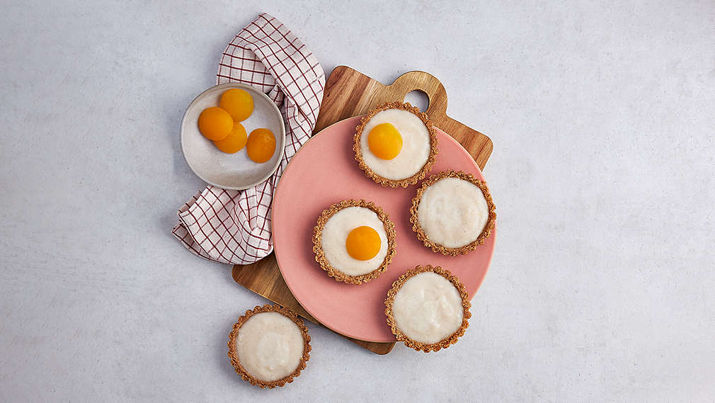 Kleine, runde, gefüllte Teigformen auf einem Holzbrett, geschmückt mit Aprikosen. Daneben ein karriertes Küchentuch sowie eine Schüssel mit Aprikosen. , Kleine, runde, gef�llte Teigformen auf einem Holzbrett, geschm�ckt mit Aprikosen. Daneben ein karriertes K�chentuch sowie eine Sch�ssel mit Aprikosen.
