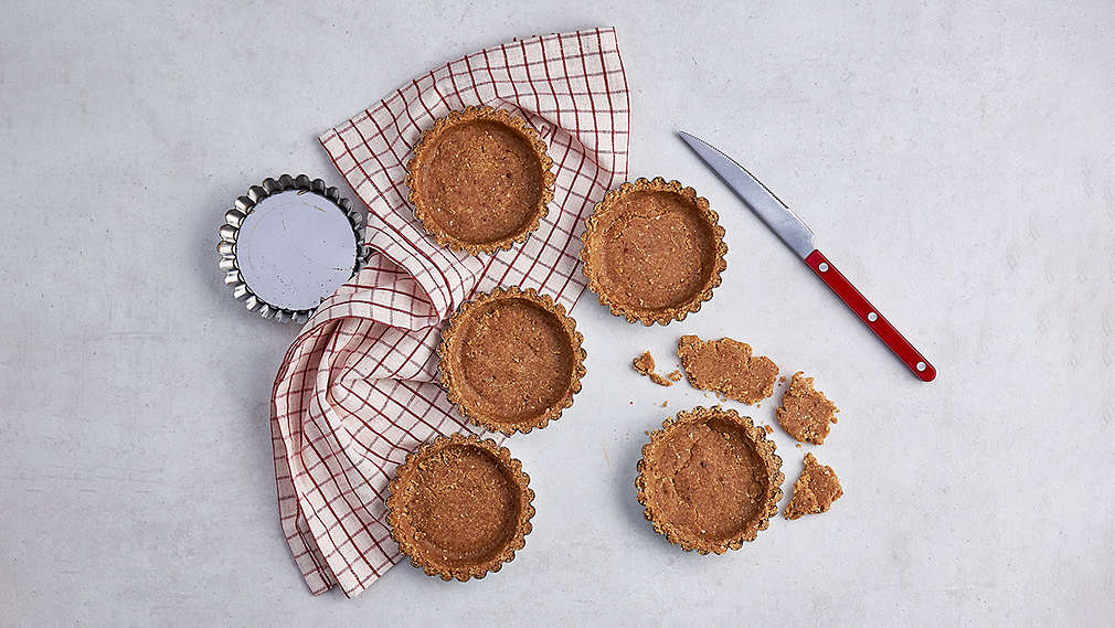 Kleine rude Teigformen auf einem karrierten Küchentuch, daneben ein rotes Messer sowie eine kleine runde Backform., Kleine rude Teigformen auf einem karrierten K�chentuch, daneben ein rotes Messer sowie eine kleine runde Backform.