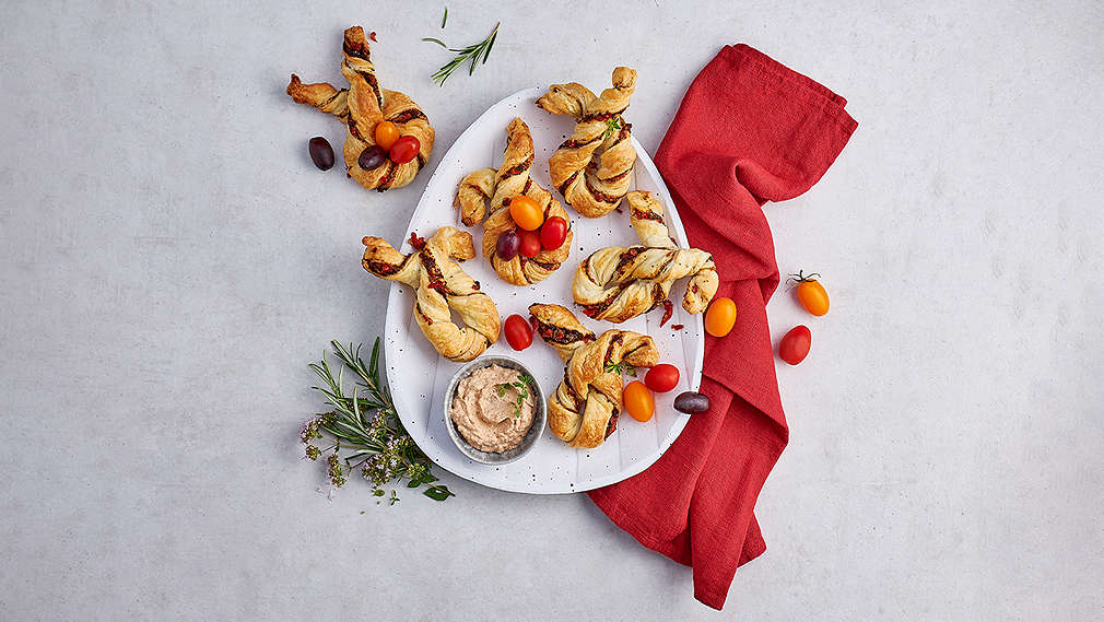 In Form von Hasen gerollte Blätterteigstangen auf einem Teller, verziert durch kleine Pralinen, Rosmarin und ein rotes Küchentuch. , In Form von Hasen gerollte Bl�tterteigstangen auf einem Teller, verziert durch kleine Pralinen, Rosmarin und ein rotes K�chentuch.