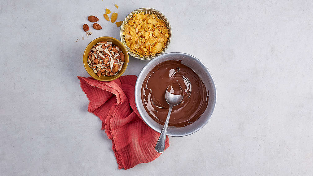 Drei Schüsseln, gefüllt mit Cornflakes, Nüssen und geschmolzener Schokolade. Daneben ein rotes Küchentuch. , Drei Sch�sseln, gef�llt mit Cornflakes, N�ssen und geschmolzener Schokolade. Daneben ein rotes K�chentuch.