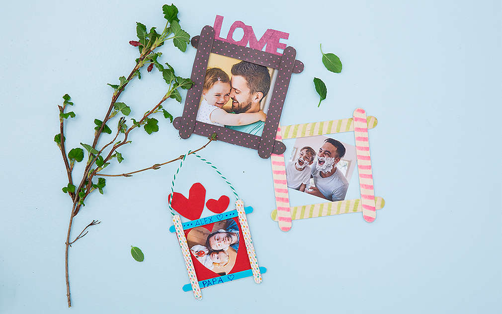 Trzy zdjęcia z własnoręcznie wykonanymi ramkami leżą na jasnoniebieskim tle, obok nich leży zielona gałązka.