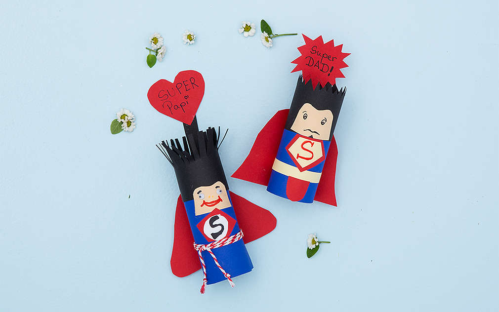 Sfotografowane z góry, dwie własnoręcznie zrobione figurki Supermana leżą na jasnoniebieskim tle.