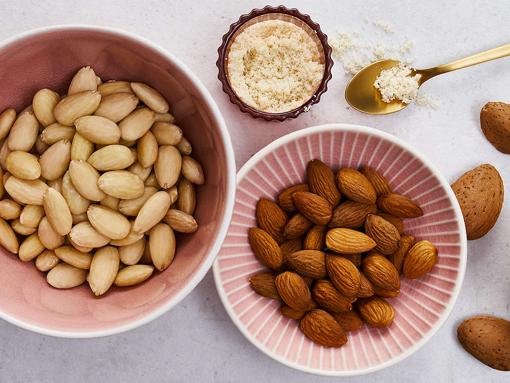 Три розовые миски с целым и молотым миндалем, рядом лежит золотая ложечка