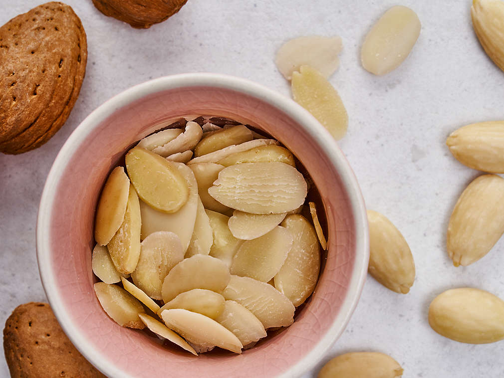 Тертый миндаль в розовой миске, рядом лежит другой миндаль