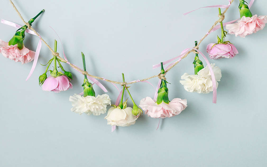 Ghirlandă din fibre naturale cu funde roz și flori albe și roz pe un fundal albastru deschis