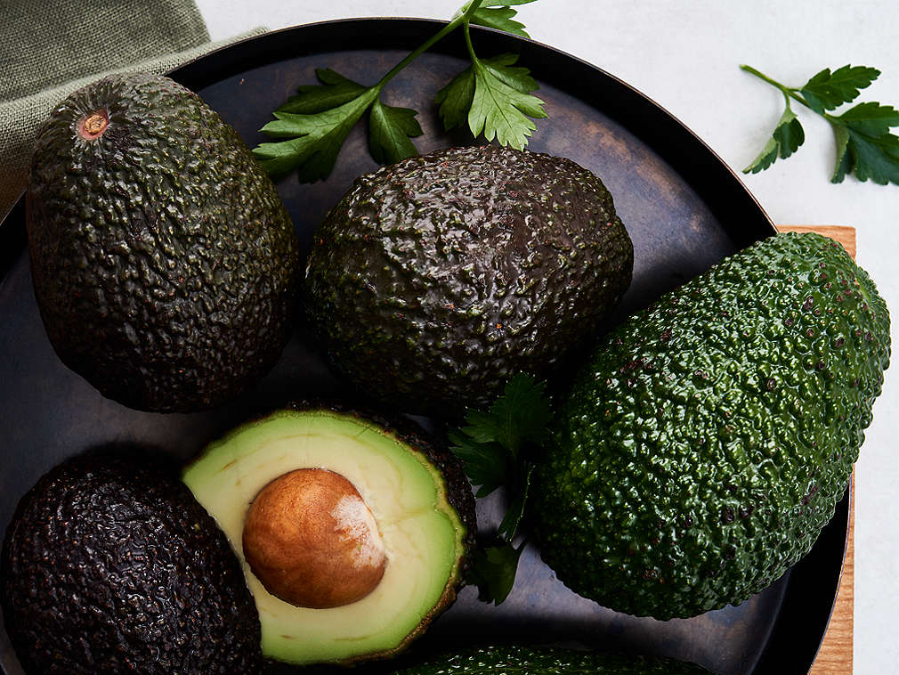Frische Avocado in der Detailansicht als Ganzes und halbiert auf einem grauen Teller 