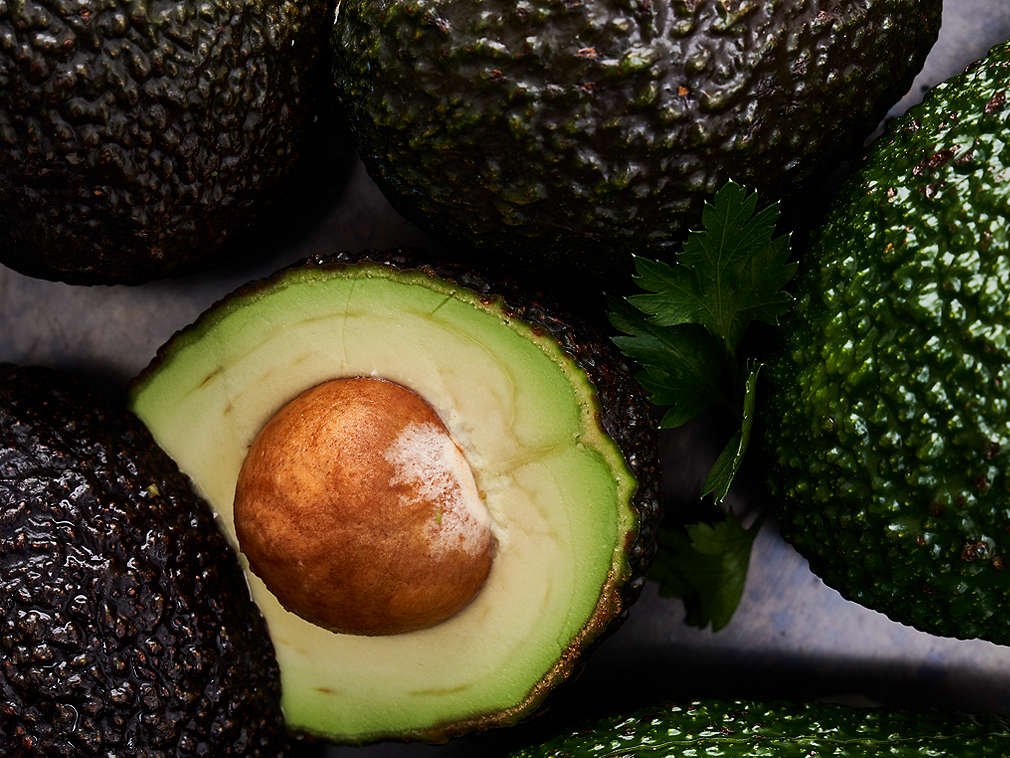 Свежее авокадо в виде целых или разрезанных наполовину фруктов, подробный вид