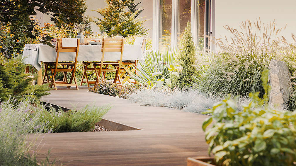 Plante și scaune de lemn așezate în jurul unei mese, pe o terasă însorită.