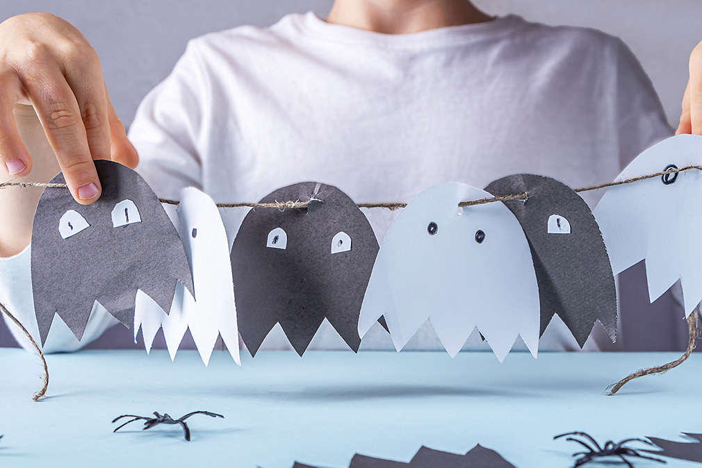 Dziecko trzyma girlandę z papierowych duszków - na przemian białego i czarnego