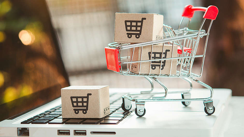 Auf einem Laptop steht ein kleiner Einkaufswagen und kleine Pakete