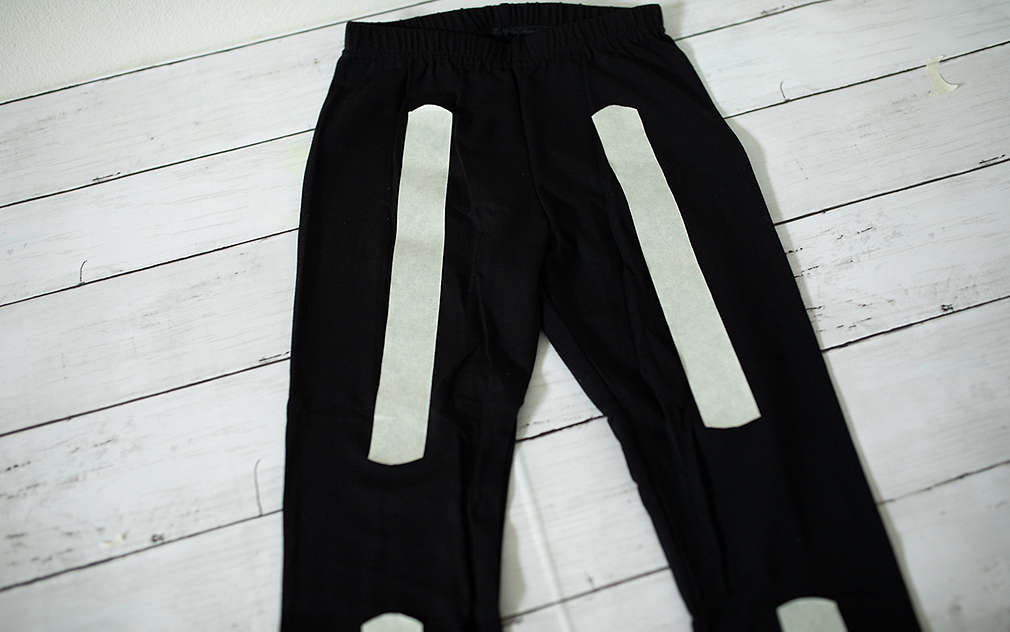 Čierne nohavice sú rozložené na svetlom podklade. Oblepené sú pásikmi z krepovej lepiacej pásky.