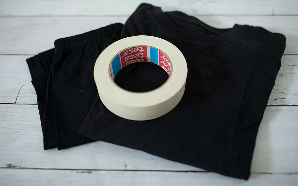 Čierne tričko a čierne nohavice, na nich je položená rolka krepovej lepiacej pásky.
