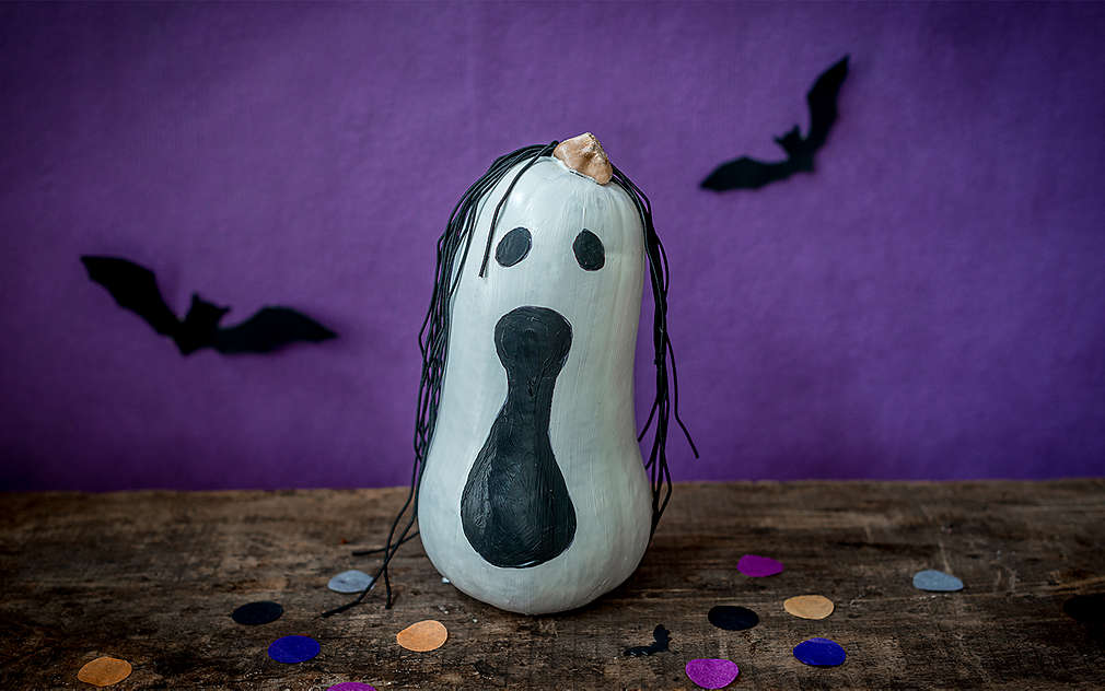 Na stole leży pomalowana na biało i czarno dynia, która wygląda jak upiorny duch.