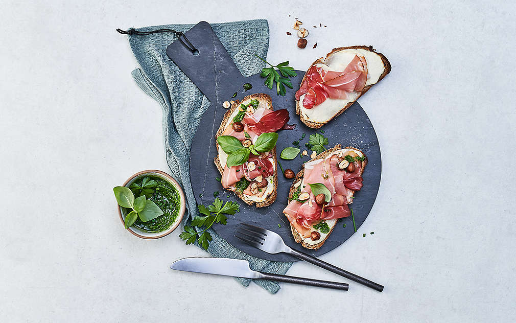 Tri kriške kruha sa svježim sirom, Schwarzwaldskom šunkom, pestom i lješnjacima.
