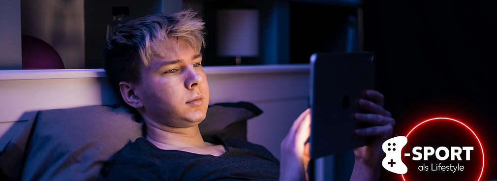 Gamer liegt im Bett und schaut auf ein Tablet, welches ihn hell anleuchtet
