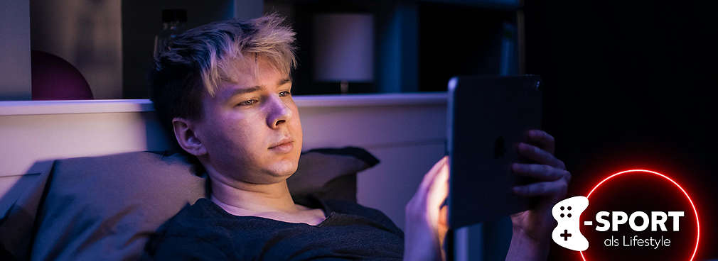 Gamer liegt im Bett und schaut auf ein Tablet, welches ihn hell anleuchtet