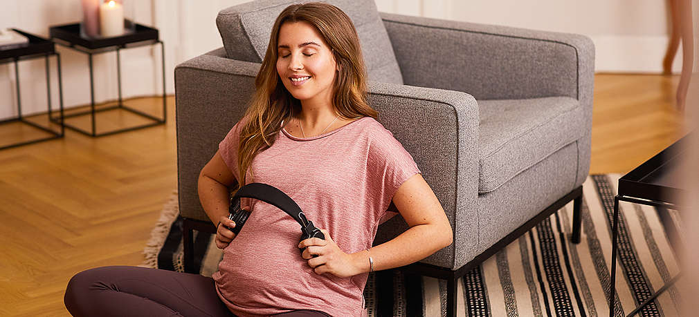 Schwangere Frau hält Kopfhörer an den Bauch