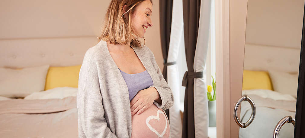 Werdende Mutter steht vor dem Spiegel und betrachtet ihren Babybauch