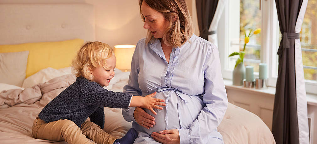 Erstgeborener legt Hand auf den Bauch seiner Mutter