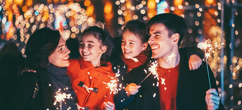 Eltern mit Kindern feiern draußen Silvester mit Wunderkerzen