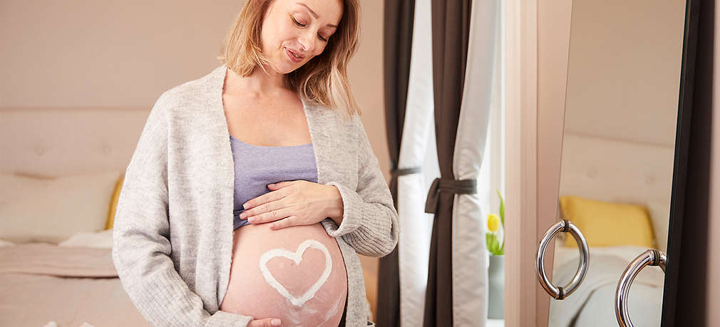 Schwangere Frau cremt Babybauch ein